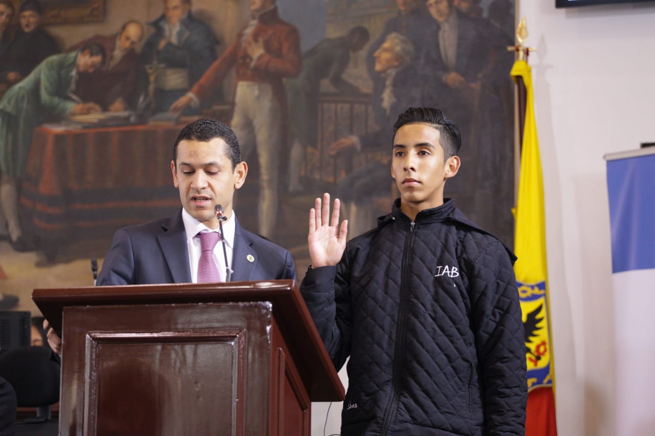 Foto de dos personas de pie, una de ellas es un adolescente con la mano derecha alzada – juramento 