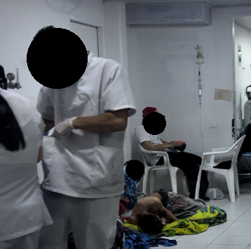 En esta fotografía se muestra un pasillo con pacientes en el piso esperando atención